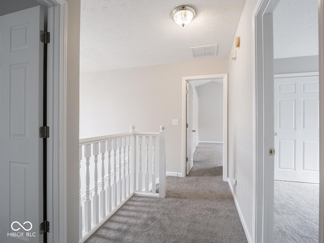 corridor with a textured ceiling, baseboards, carpet flooring, and an upstairs landing