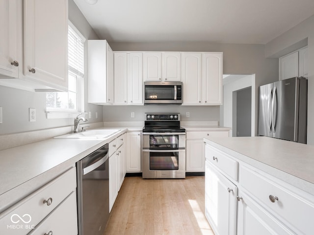 kitchen featuring light countertops, appliances with stainless steel finishes, white cabinetry, a sink, and light wood-type flooring