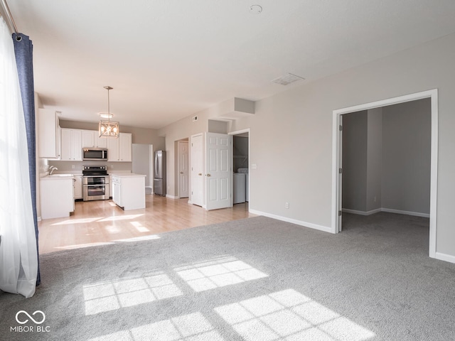 unfurnished living room with washer / dryer, light carpet, and baseboards