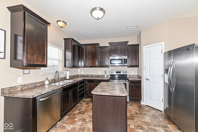 kitchen with visible vents, appliances with stainless steel finishes, stone finish flooring, a kitchen island, and a sink