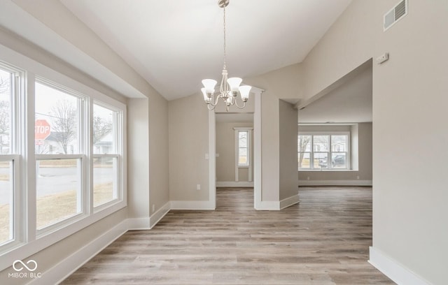 unfurnished dining area featuring a chandelier, vaulted ceiling, and light hardwood / wood-style flooring