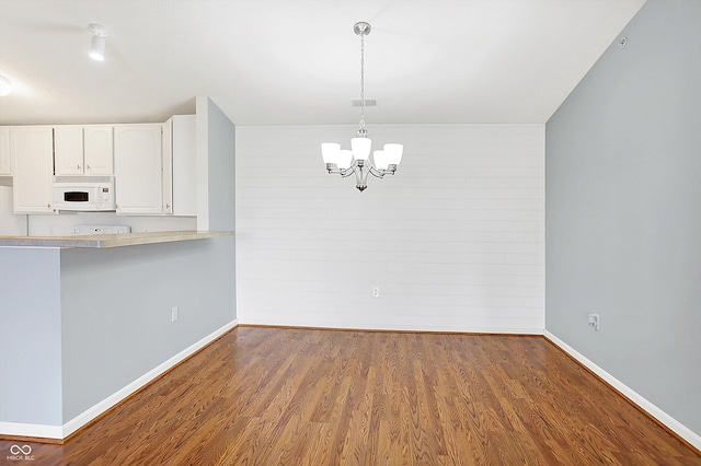 unfurnished dining area with baseboards, visible vents, an inviting chandelier, and wood finished floors