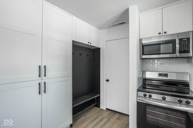 kitchen with light wood-type flooring, appliances with stainless steel finishes, white cabinetry, and tasteful backsplash