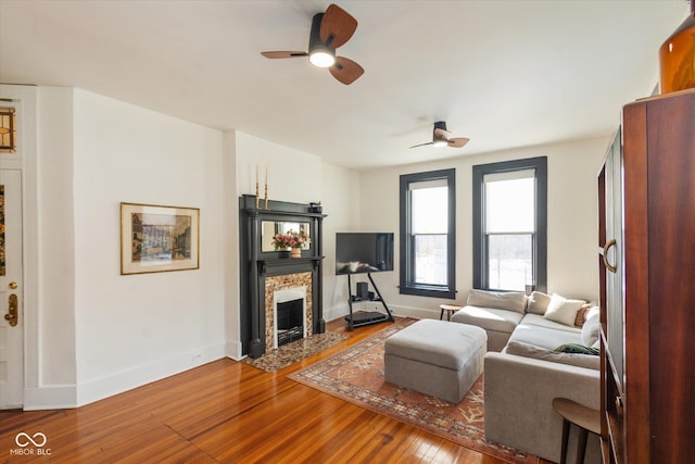 living area featuring ceiling fan, a fireplace, wood finished floors, and baseboards