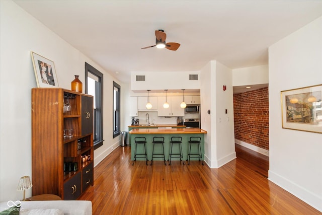 kitchen with decorative light fixtures, visible vents, wooden counters, appliances with stainless steel finishes, and a kitchen bar