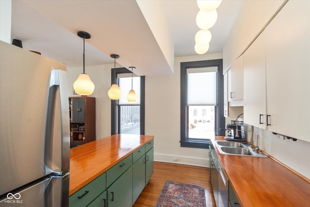 kitchen featuring dark wood finished floors, hanging light fixtures, appliances with stainless steel finishes, white cabinetry, and a sink