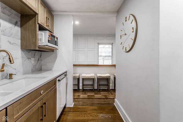 kitchen featuring sink, backsplash, light stone countertops, dark wood-type flooring, and white appliances