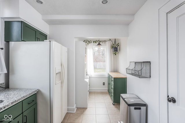 kitchen featuring light tile patterned floors, white refrigerator with ice dispenser, baseboards, green cabinets, and light stone countertops