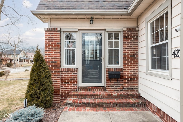 property entrance featuring brick siding and roof with shingles