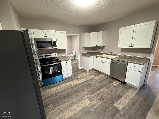 kitchen featuring appliances with stainless steel finishes, dark hardwood / wood-style floors, sink, white cabinets, and a textured ceiling