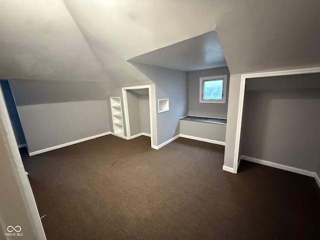 additional living space with built in shelves, dark carpet, and vaulted ceiling