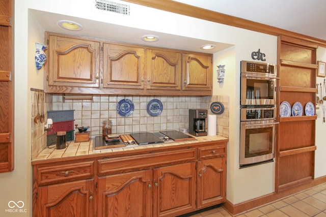 kitchen featuring brown cabinets, tile counters, visible vents, backsplash, and appliances with stainless steel finishes