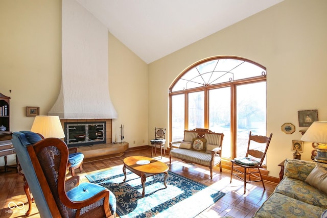 living room with high vaulted ceiling, a tile fireplace, baseboards, and wood finished floors