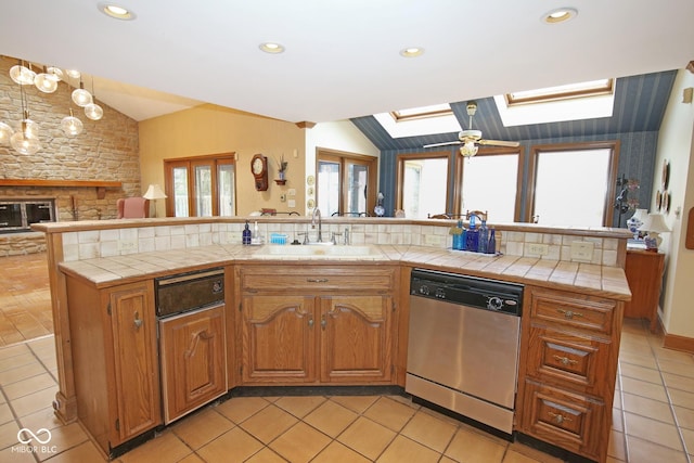 kitchen with dishwasher, tile countertops, lofted ceiling with skylight, a fireplace, and a sink