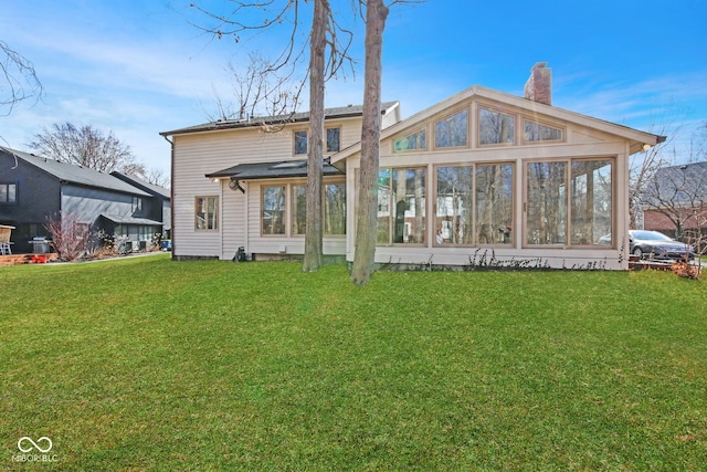 rear view of house featuring a sunroom, a lawn, and a chimney