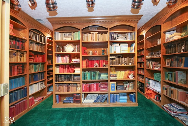 interior space with wall of books, carpet, and a textured ceiling