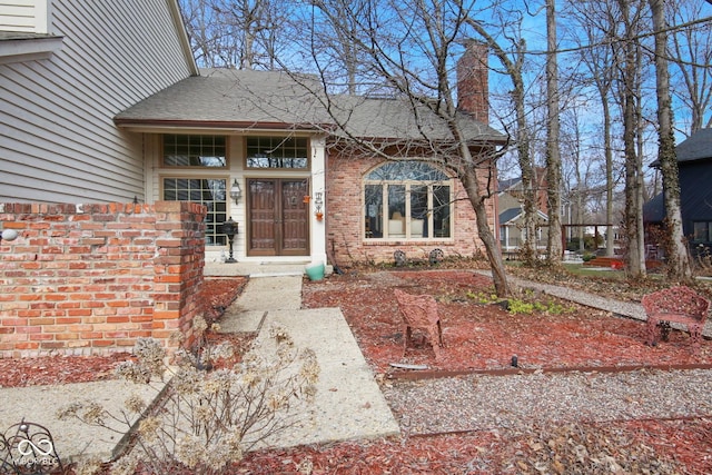 entrance to property featuring roof with shingles, brick siding, and a chimney