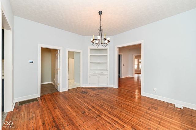 unfurnished dining area featuring hardwood / wood-style flooring, a textured ceiling, built in features, and a chandelier