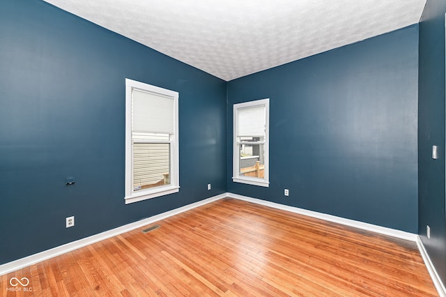 empty room with a textured ceiling and light hardwood / wood-style flooring