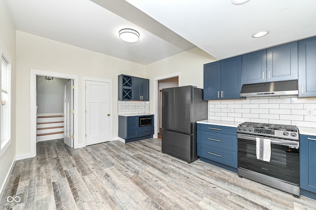 kitchen with tasteful backsplash, appliances with stainless steel finishes, blue cabinets, and light wood-type flooring