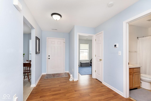 hall with visible vents, light wood-style flooring, and baseboards