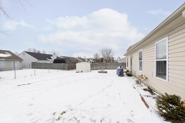 yard layered in snow featuring a fenced backyard, a storage unit, and an outbuilding