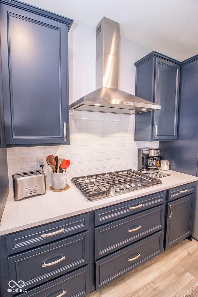 kitchen with light wood-type flooring, stainless steel gas cooktop, backsplash, and wall chimney exhaust hood