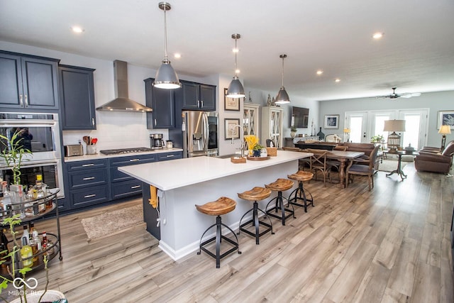 kitchen with appliances with stainless steel finishes, wall chimney exhaust hood, a kitchen bar, and a kitchen island with sink