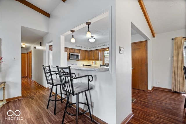 kitchen featuring stainless steel microwave, brown cabinetry, dark wood-style flooring, and light countertops