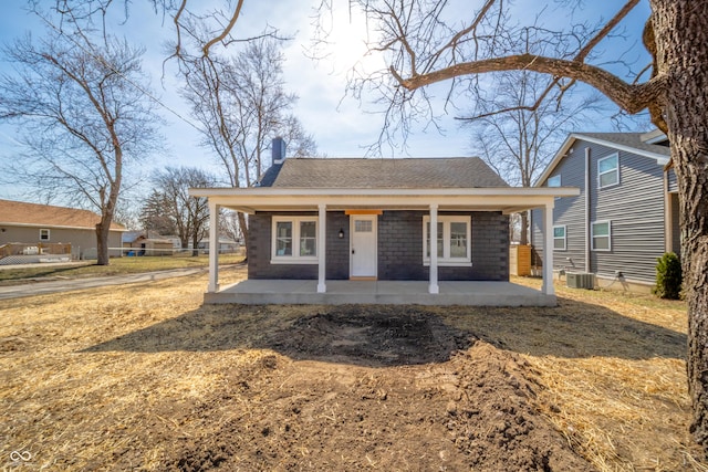 view of front facade featuring a porch, cooling unit, roof with shingles, and a chimney