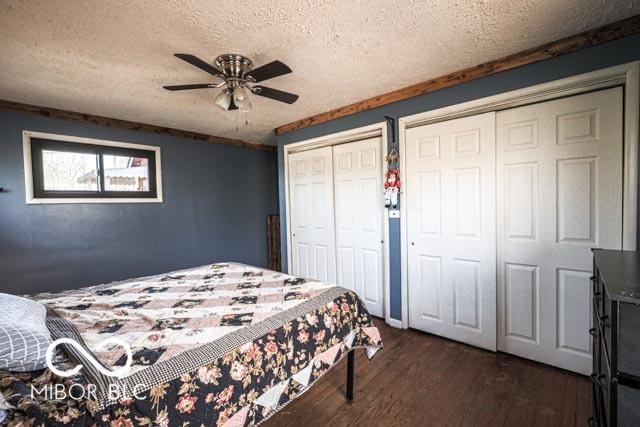 bedroom featuring ceiling fan, dark hardwood / wood-style floors, two closets, and a textured ceiling