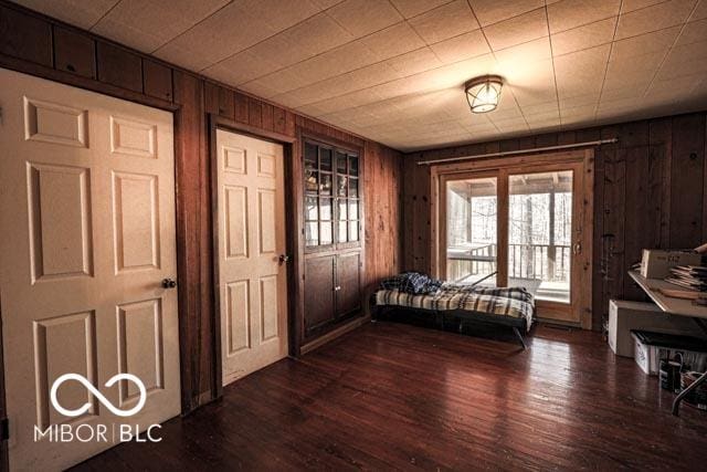 bedroom with wooden walls, dark hardwood / wood-style floors, and access to exterior