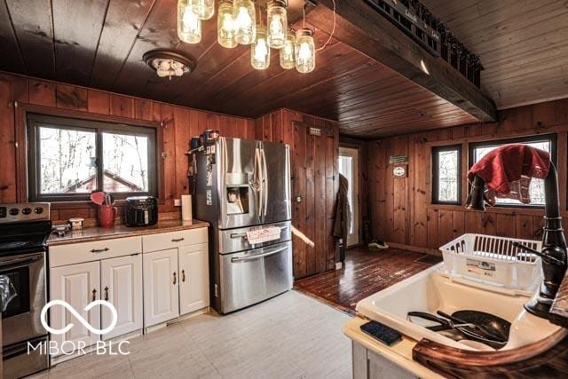 kitchen with appliances with stainless steel finishes, a wealth of natural light, wooden ceiling, and wood walls