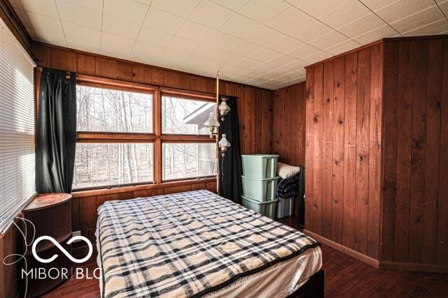 bedroom with multiple windows, wooden walls, and dark hardwood / wood-style floors