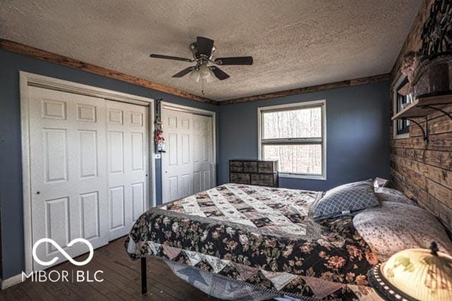 bedroom featuring two closets, hardwood / wood-style floors, a textured ceiling, and ceiling fan