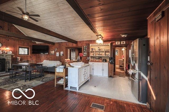 kitchen with white cabinetry, dark hardwood / wood-style flooring, stainless steel fridge, and wood walls