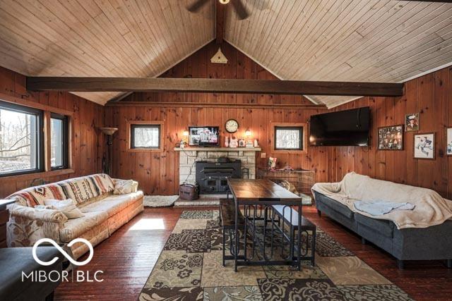 living room with hardwood / wood-style flooring, vaulted ceiling with beams, ceiling fan, and wood walls