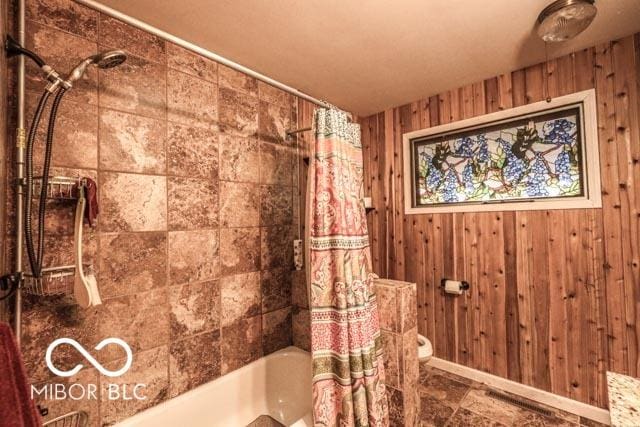 bathroom featuring toilet, shower / tub combo with curtain, and wood walls