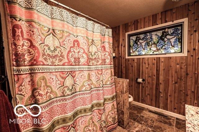 bathroom with a textured ceiling, toilet, and wood walls