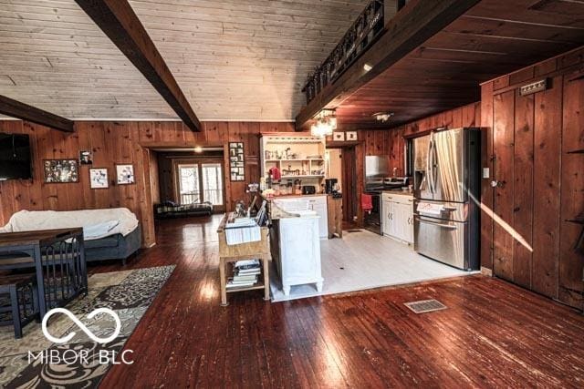 kitchen featuring dark hardwood / wood-style floors, wooden walls, beamed ceiling, stainless steel refrigerator with ice dispenser, and wooden ceiling