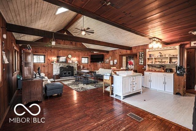 living room featuring vaulted ceiling with beams, ceiling fan, hardwood / wood-style floors, and wood walls