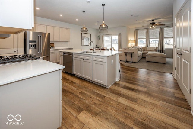 kitchen with pendant lighting, an island with sink, sink, white cabinets, and stainless steel appliances