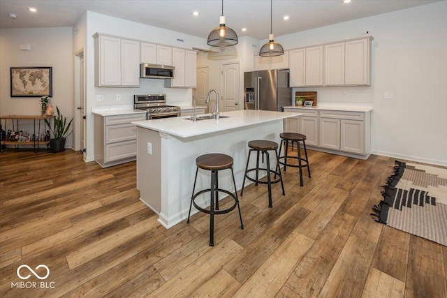 kitchen with sink, decorative light fixtures, light wood-type flooring, appliances with stainless steel finishes, and an island with sink