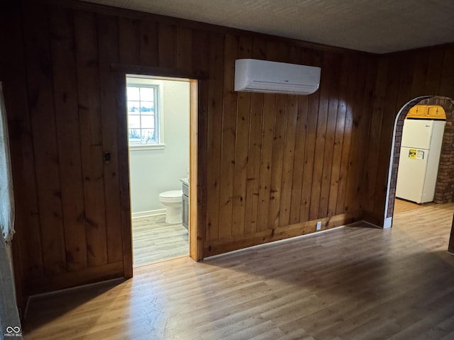 unfurnished dining area featuring light wood-type flooring, wooden walls, and a wall unit AC