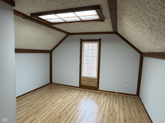 additional living space featuring lofted ceiling, a textured ceiling, and light hardwood / wood-style flooring