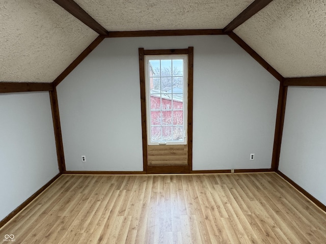 additional living space featuring lofted ceiling with beams, a textured ceiling, and light wood-type flooring