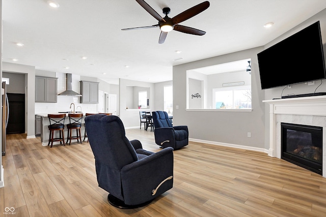 living room with light wood-type flooring, baseboards, ceiling fan, and a premium fireplace