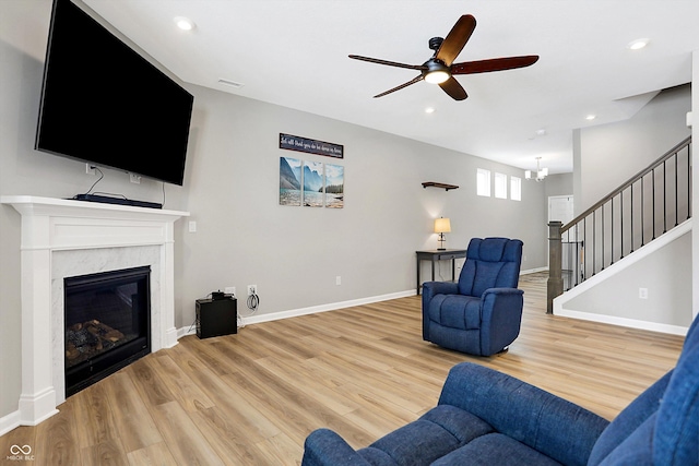 living area with light wood finished floors, ceiling fan with notable chandelier, stairway, and a fireplace