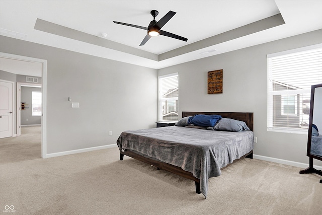 bedroom with a ceiling fan, visible vents, light colored carpet, baseboards, and a tray ceiling