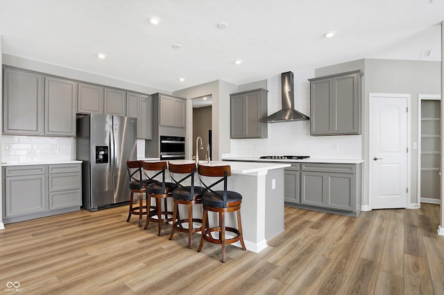 kitchen featuring gray cabinetry, appliances with stainless steel finishes, wall chimney exhaust hood, and light wood-type flooring